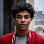 Portrait of a young man in a red jacket, captured in an urban setting with a solemn expression.