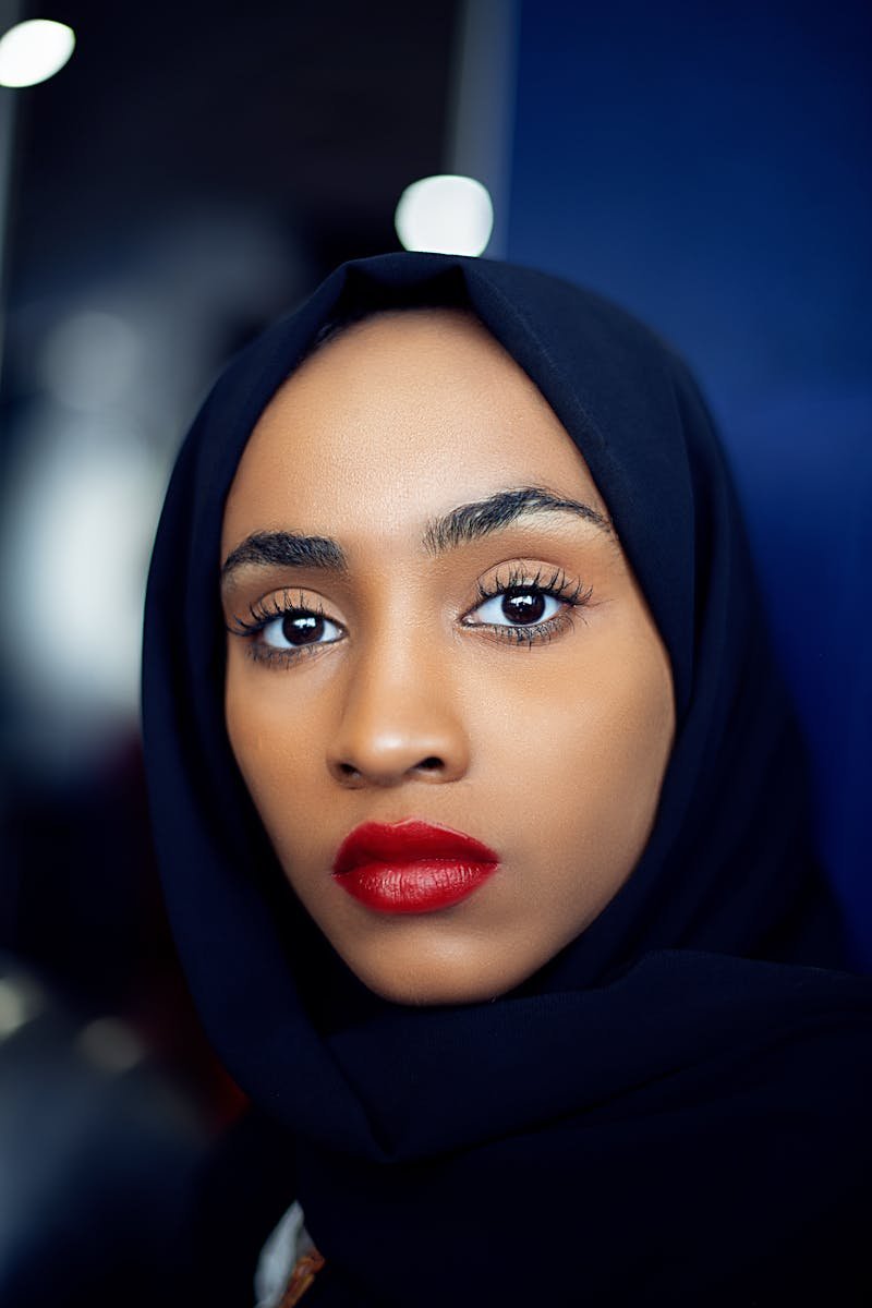 Close-up portrait of a woman with red lipstick and black hijab, exuding elegance.